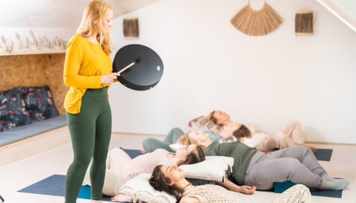 Group therapy session with Tibetan drum for group of women lying on wooden floor surrounded by copper bowls. Meditation and relaxation
